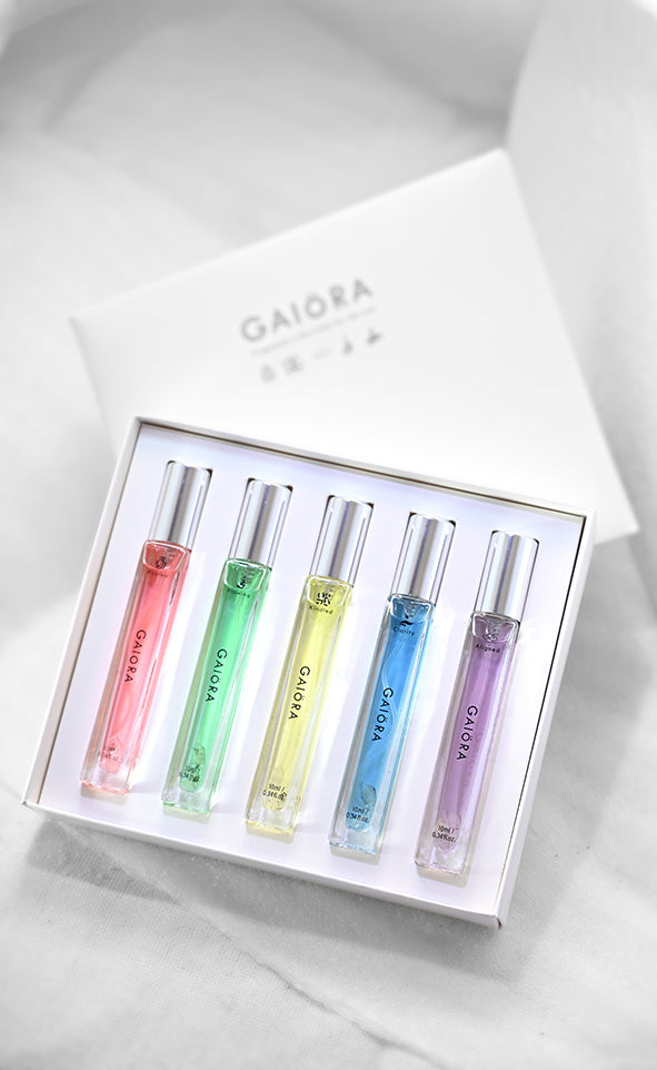 A boxed set of five GAIORA fragrance sample vials in pastel pink, green, yellow, blue, and purple, arranged in a white presentation box on a light marble-like surface.